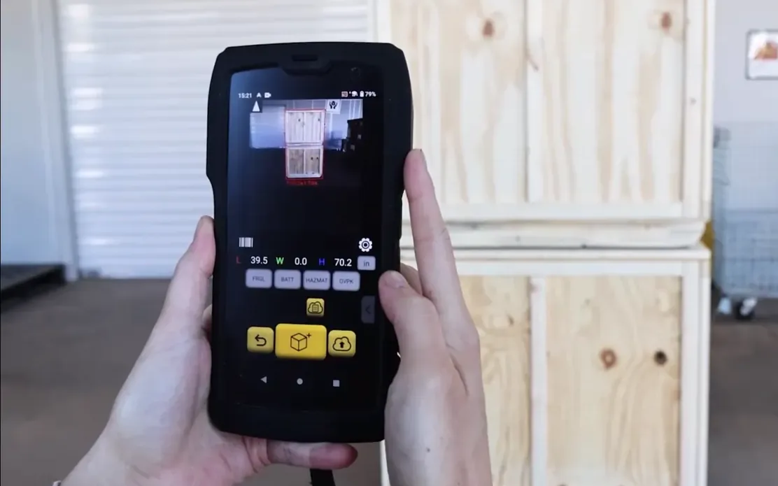 Hands holding the M2 up to a pair of stacked crates, with the measurement on its screen